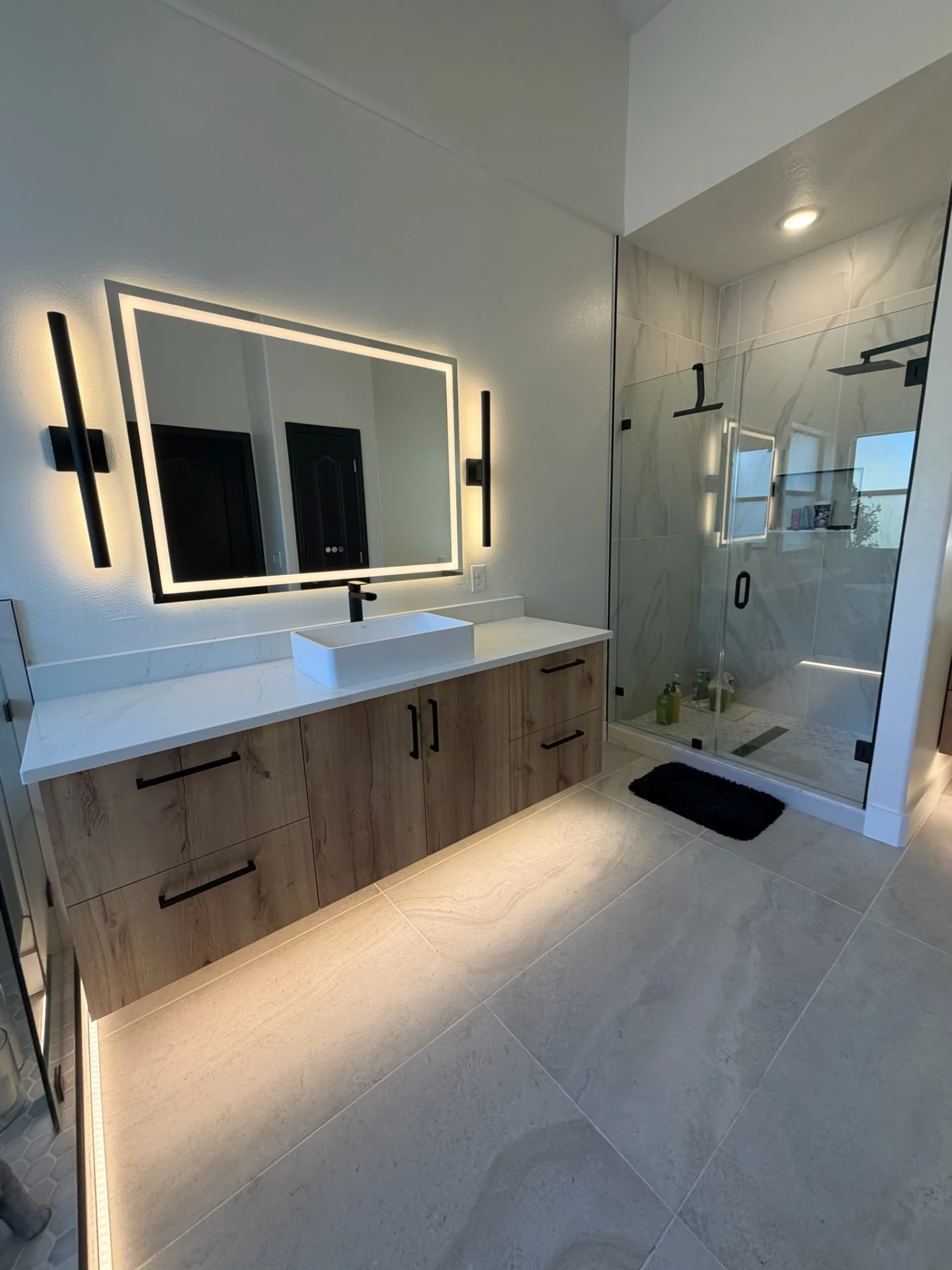 Remodeled bathroom with light wood floating vanity, white vessel sink, backlit LED mirror and glass walk-in shower