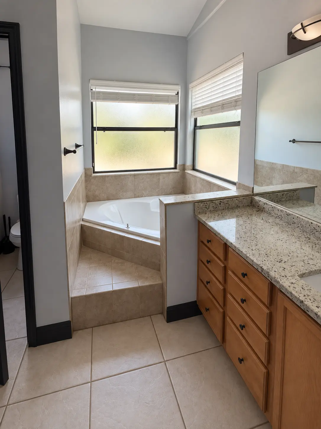 Dated bathroom with corner tub, beige tile and oak vanity before remodeling