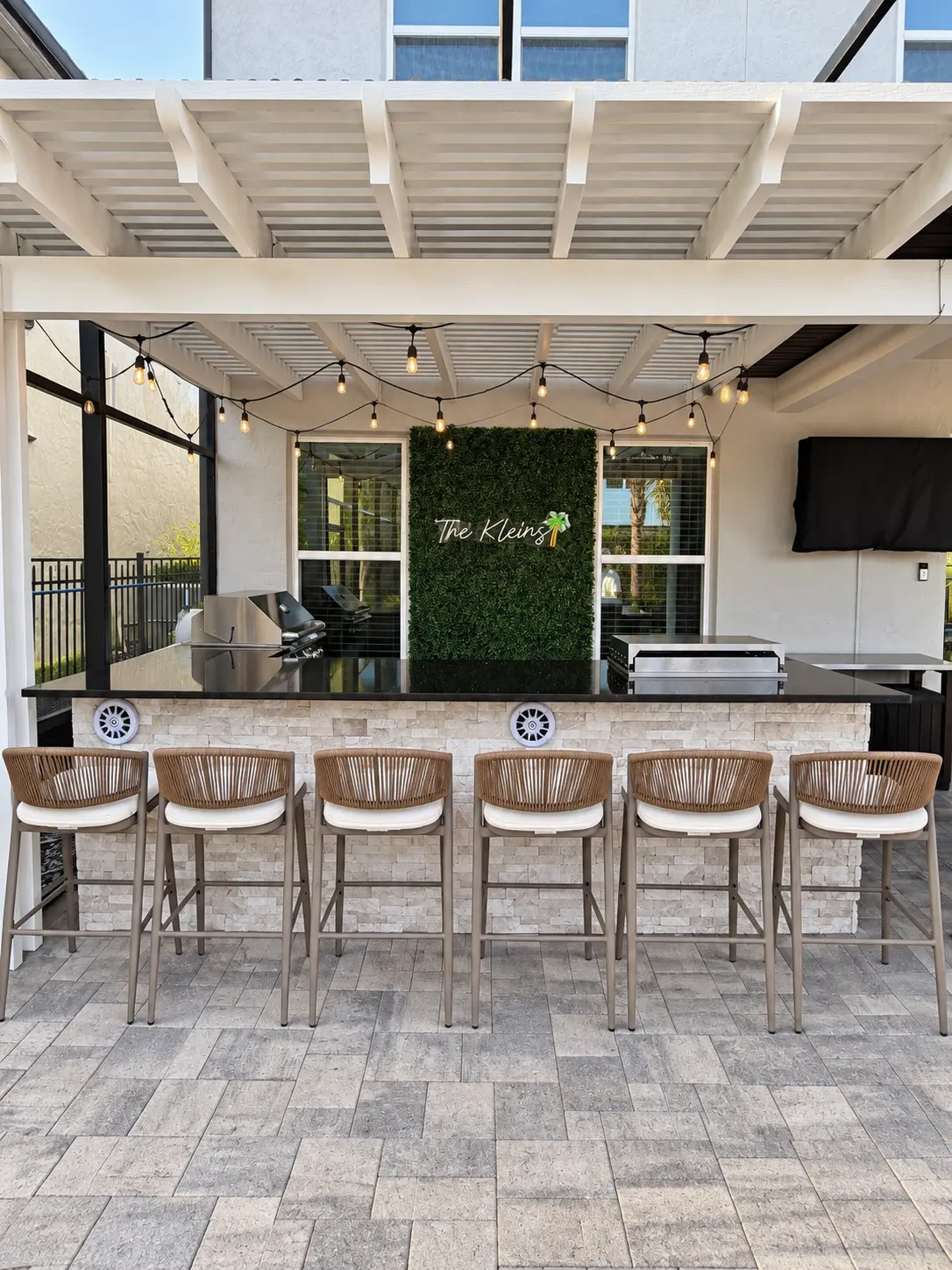 Covered outdoor kitchen with black granite bar, grill, greenery wall and string lights